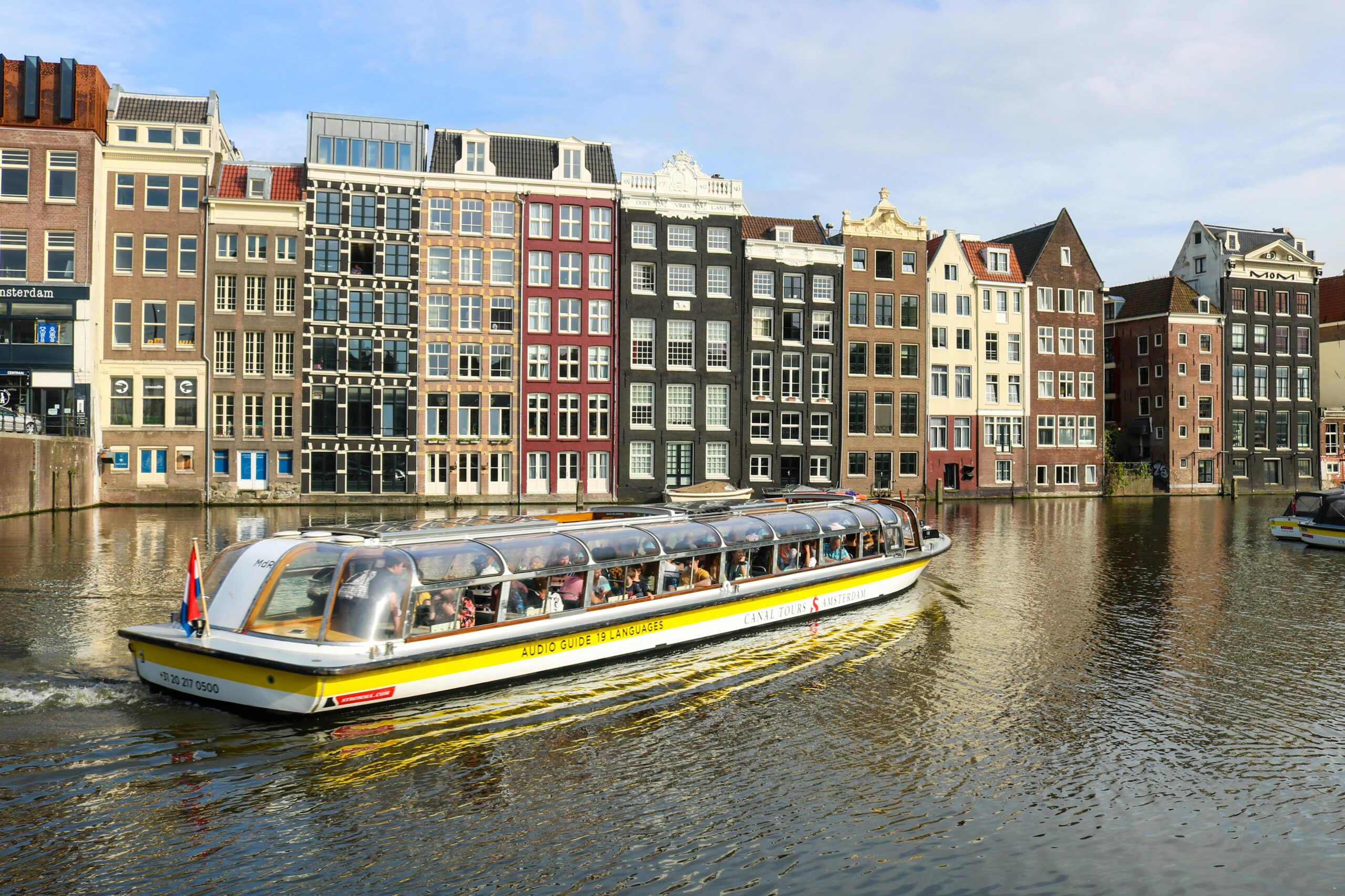 A vibrant canal in Amsterdam featuring a tour boat and iconic canal houses under a clear blue sky.