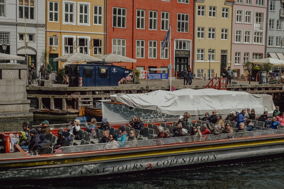 Tourists enjoying a scenic canal tour in Copenhagen, Denmark, with vibrant waterfront buildings.